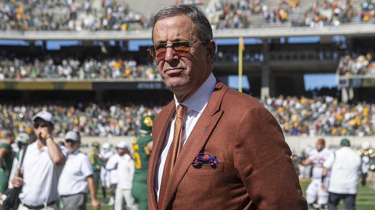 Texas athletics director Chris Del Conte stands on the field in a burnt orange jacket after a game.