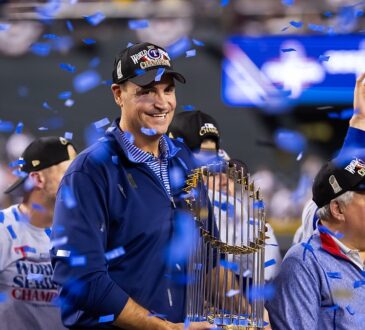 Rangers executive Chris Young smiles and holds the Commissioner's Trophy as blue confetti falls around him.
