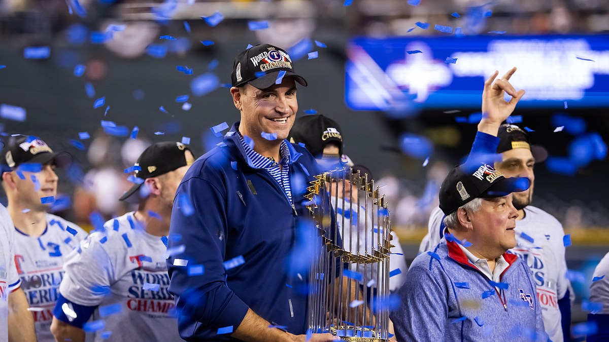 Rangers executive Chris Young smiles and holds the Commissioner's Trophy as blue confetti falls around him.