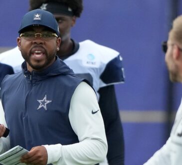 Dallas Cowboys defensive coordinator Christian Parker talks while holding a radio and a call sheet at a joint practice.
