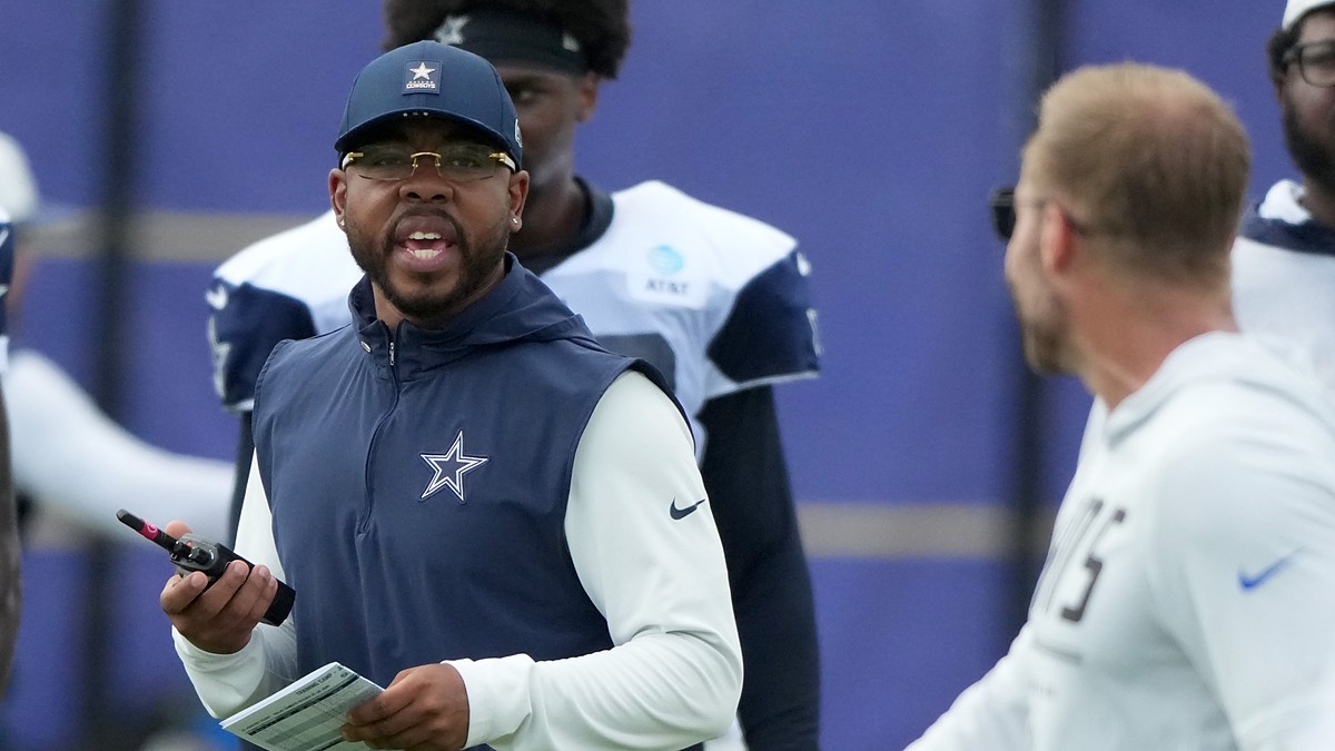 Dallas Cowboys defensive coordinator Christian Parker talks while holding a radio and a call sheet at a joint practice.