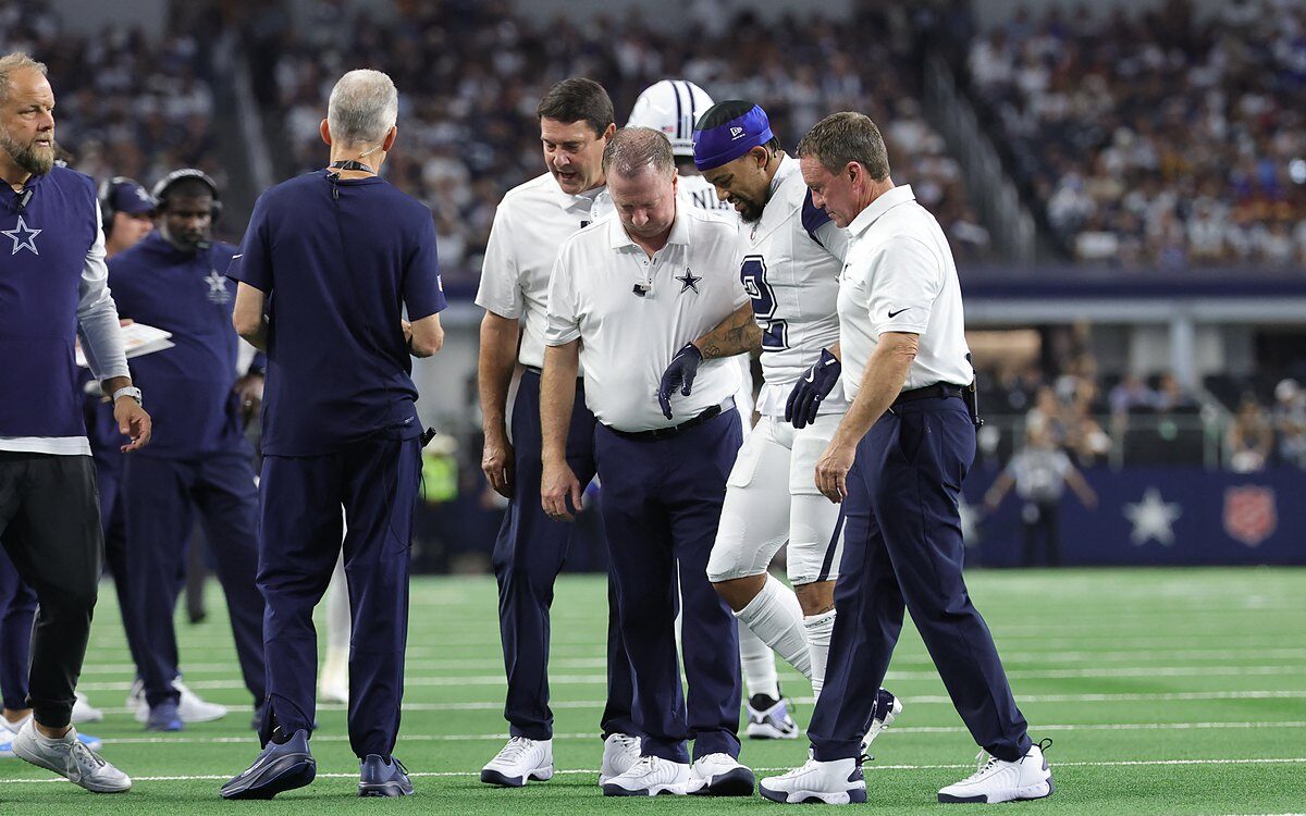 Dallas Cowboys cornerback Cobie Durant walks off the field with team staff on either side of him.