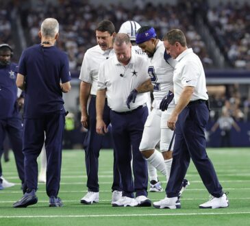 Dallas Cowboys cornerback Cobie Durant walks off the field with team staff on either side of him.