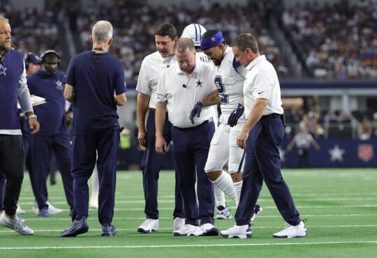 Dallas Cowboys cornerback Cobie Durant walks off the field with team staff on either side of him.