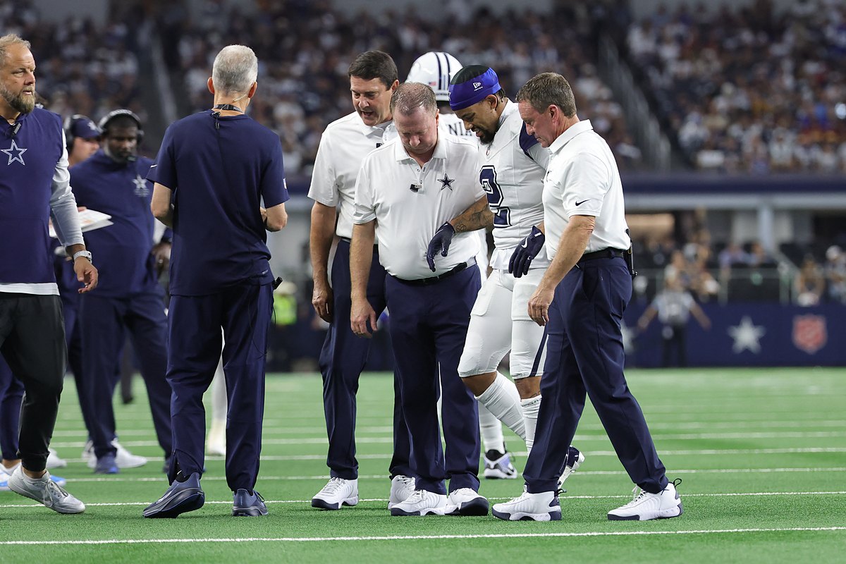 Dallas Cowboys cornerback Cobie Durant walks off the field with team staff on either side of him.