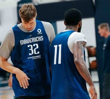Dallas Mavericks forward Cooper Flagg and guard Kyrie Irving walk side by side in blue practice jerseys during a team practice.