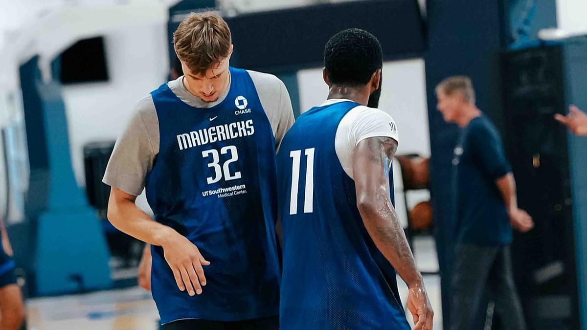 Dallas Mavericks forward Cooper Flagg and guard Kyrie Irving walk side by side in blue practice jerseys during a team practice.