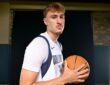 Dallas Mavericks forward Cooper Flagg holds a basketball at his chest and looks toward the camera in a white home jersey.