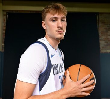 Dallas Mavericks forward Cooper Flagg holds a basketball at his chest and looks toward the camera in a white home jersey.