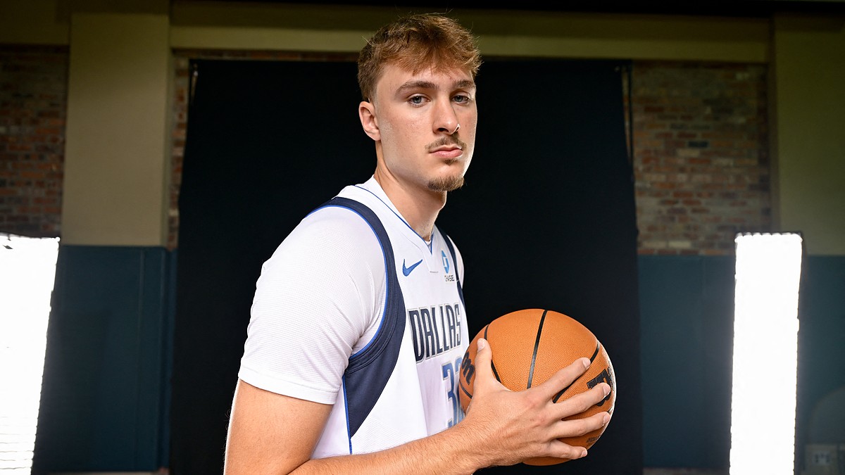 Dallas Mavericks forward Cooper Flagg holds a basketball at his chest and looks toward the camera in a white home jersey.