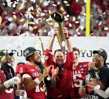 Indiana Hoosiers head coach Curt Cignetti raises the College Football Playoff trophy as players celebrate around him.