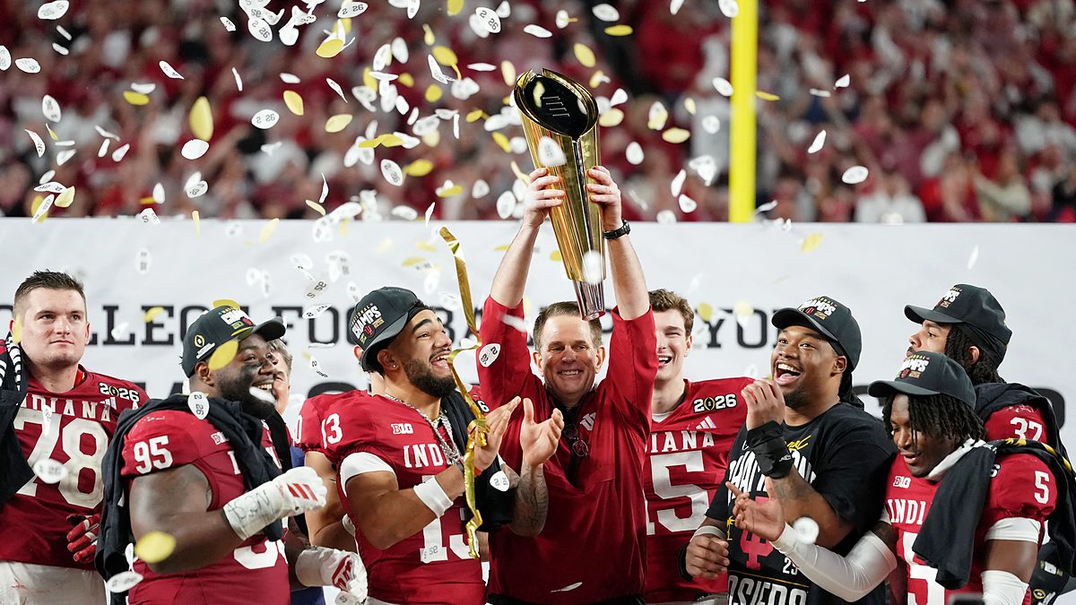 Indiana Hoosiers head coach Curt Cignetti raises the College Football Playoff trophy as players celebrate around him.