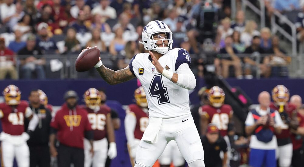 Dallas Cowboys quarterback Dak Prescott cocks his arm to throw from the pocket with the Commanders sideline behind him.
