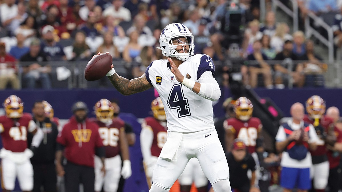 Dallas Cowboys quarterback Dak Prescott cocks his arm to throw from the pocket with the Commanders sideline behind him.