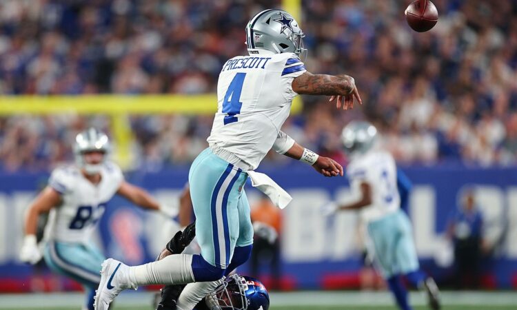 Dallas Cowboys quarterback Dak Prescott releases a pass as a New York Giants defender tackles him low.