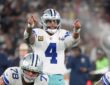 Dallas Cowboys quarterback Dak Prescott points with both hands at the line of scrimmage behind two offensive linemen.