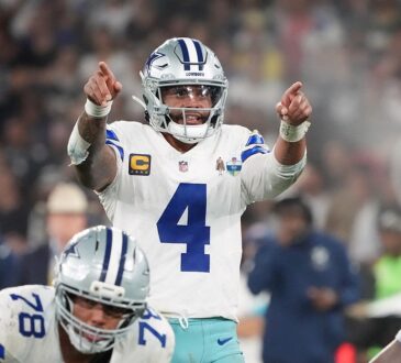 Dallas Cowboys quarterback Dak Prescott points with both hands at the line of scrimmage behind two offensive linemen.