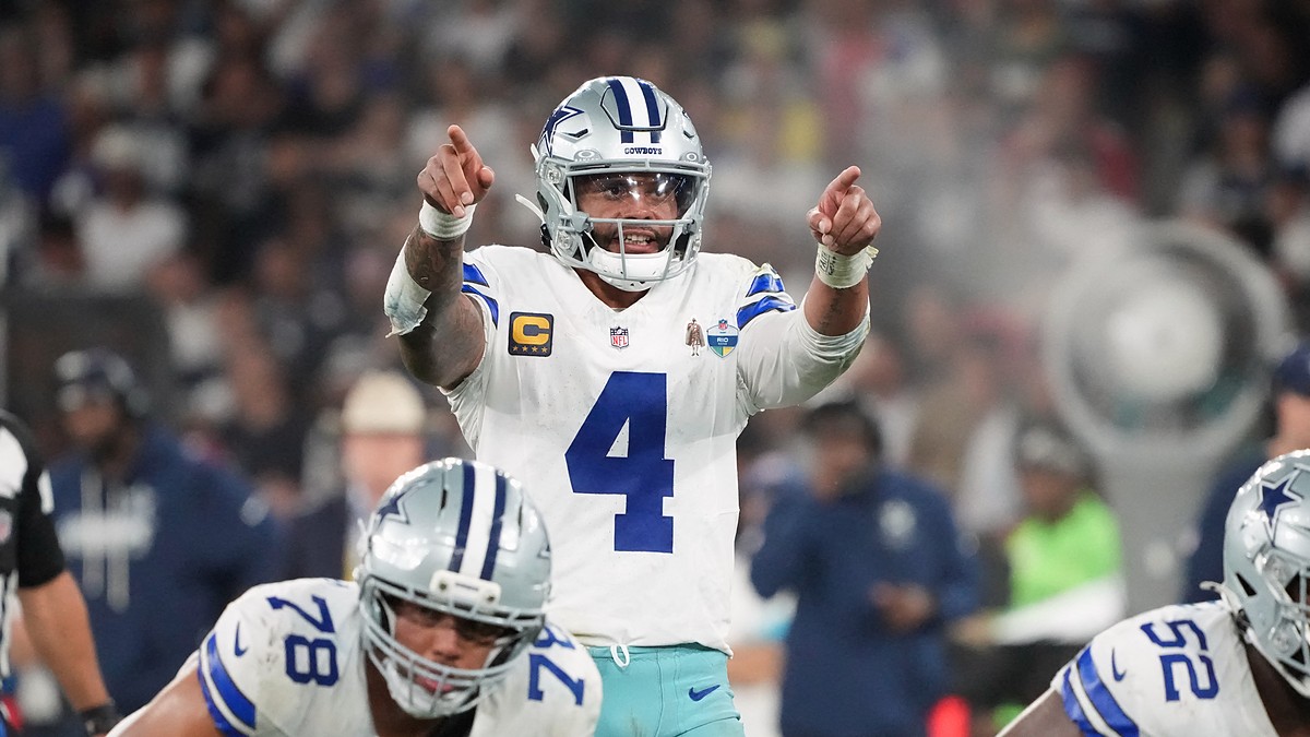 Dallas Cowboys quarterback Dak Prescott points with both hands at the line of scrimmage behind two offensive linemen.