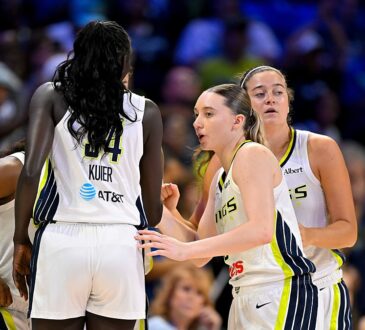 Dallas Wings players huddle on the court in white home uniforms before a game.