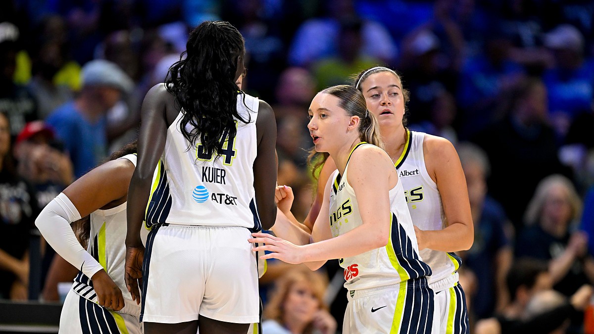 Dallas Wings players huddle on the court in white home uniforms before a game.