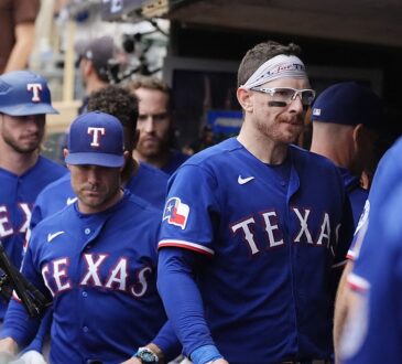 Texas Rangers catcher Danny Jansen, wearing a headband and sport glasses, walks through the dugout with his teammates.