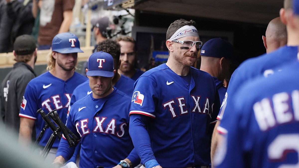 Texas Rangers catcher Danny Jansen, wearing a headband and sport glasses, walks through the dugout with his teammates.