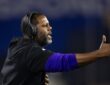 Coach Daronte Jones extends an arm and calls out instructions from the sideline in a headset.