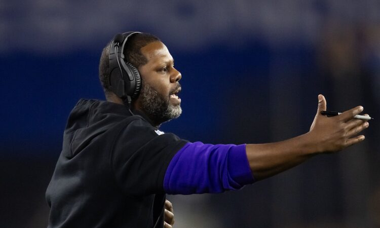 Coach Daronte Jones extends an arm and calls out instructions from the sideline in a headset.