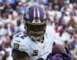 Baltimore Ravens running back Derrick Henry clutches the ball with both hands as he runs upfield.