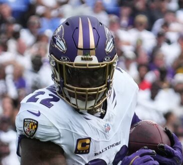 Baltimore Ravens running back Derrick Henry clutches the ball with both hands as he runs upfield.