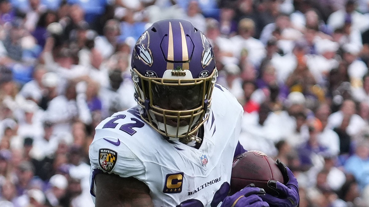 Baltimore Ravens running back Derrick Henry clutches the ball with both hands as he runs upfield.