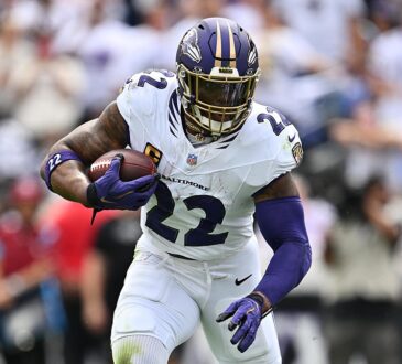 Baltimore Ravens running back Derrick Henry carries the ball upfield with a teammate blocking to his left.