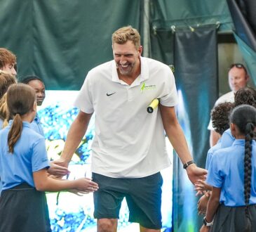 Former Dallas Mavericks forward Dirk Nowitzki smiles and slaps hands with children lining both sides of a tennis court.