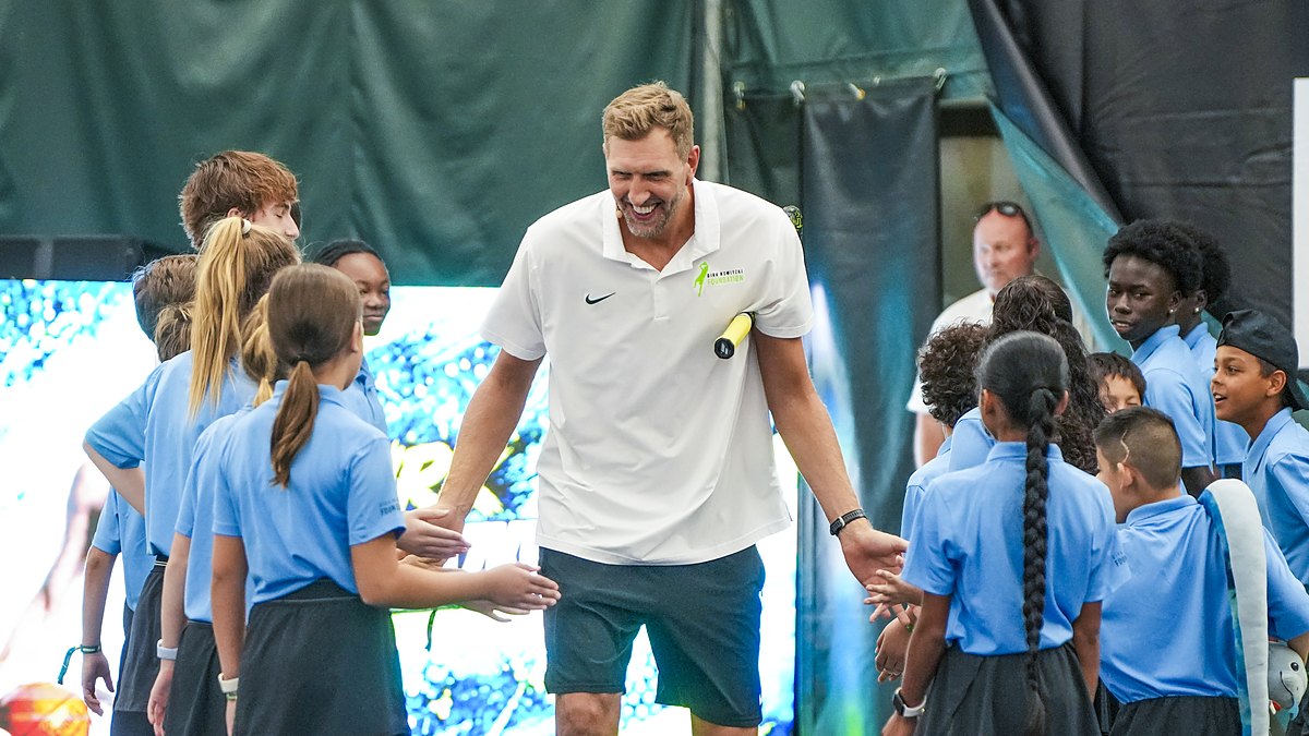 Former Dallas Mavericks forward Dirk Nowitzki smiles and slaps hands with children lining both sides of a tennis court.