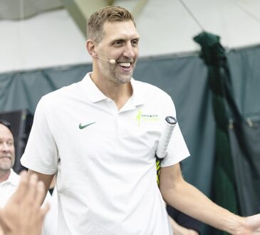 Former Dallas Mavericks forward Dirk Nowitzki smiles and high-fives a line of fans with a tennis racket tucked under his arm.