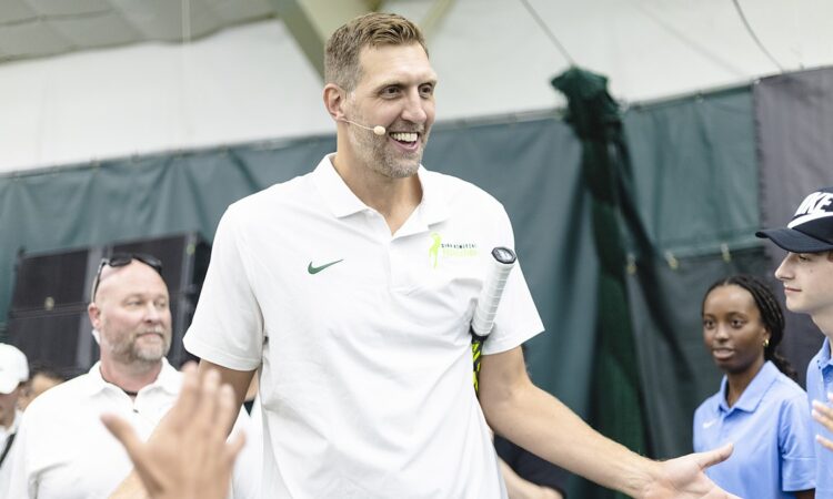 Former Dallas Mavericks forward Dirk Nowitzki smiles and high-fives a line of fans with a tennis racket tucked under his arm.