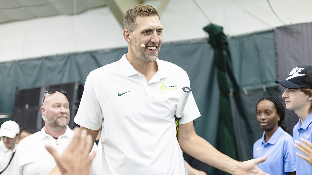Former Dallas Mavericks forward Dirk Nowitzki smiles and high-fives a line of fans with a tennis racket tucked under his arm.