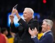 Former Dallas Mavericks coach Don Nelson smiles and raises a crystal trophy as a man beside him applauds.