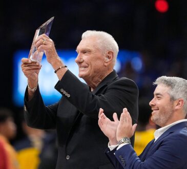 Former Dallas Mavericks coach Don Nelson smiles and raises a crystal trophy as a man beside him applauds.