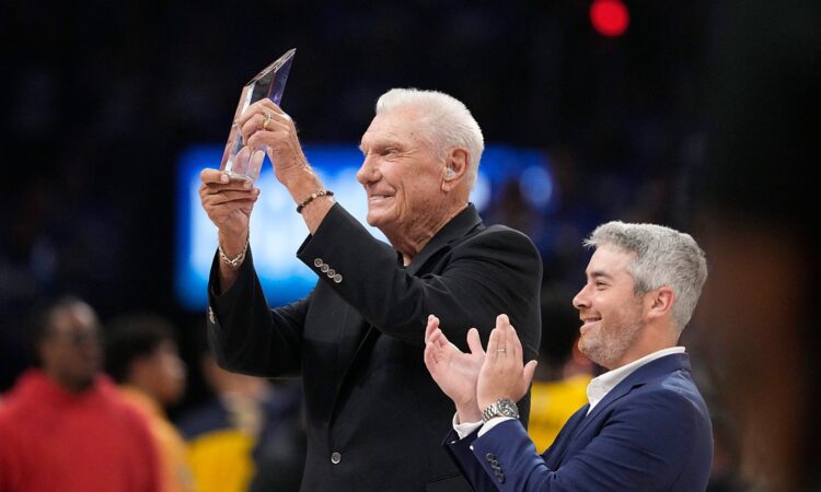 Former Dallas Mavericks coach Don Nelson smiles and raises a crystal trophy as a man beside him applauds.