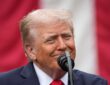 President Donald Trump speaks at a microphone in front of an American flag at a Pentagon memorial event.