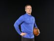 Dallas Mavericks head coach Dusty May stands with a hand on his hip and a basketball under his arm.