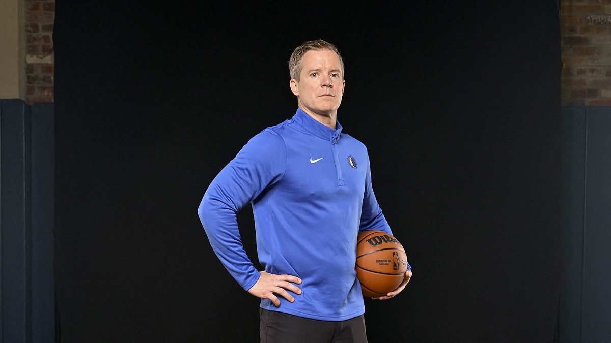 Dallas Mavericks head coach Dusty May stands with a hand on his hip and a basketball under his arm.