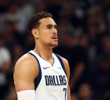 Dallas Mavericks forward Dwight Powell looks on during a game in his white Dallas jersey with a sleeve on his right arm.