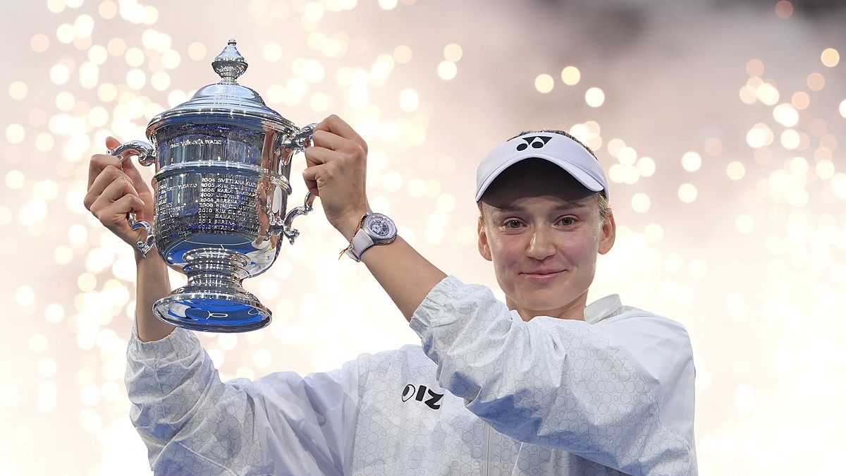 Elena Rybakina raises the U.S. Open trophy overhead as sparks fall behind her.
