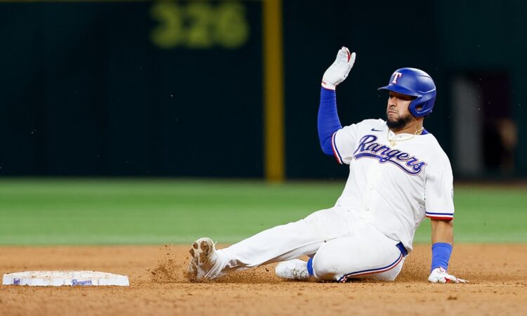Texas Rangers catcher Elias Díaz slides into second base with his glove hand raised as dirt kicks up.