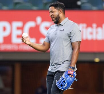 Former Texas Rangers shortstop Elvis Andrus smiles while holding a baseball and wearing a blue glove on the field.