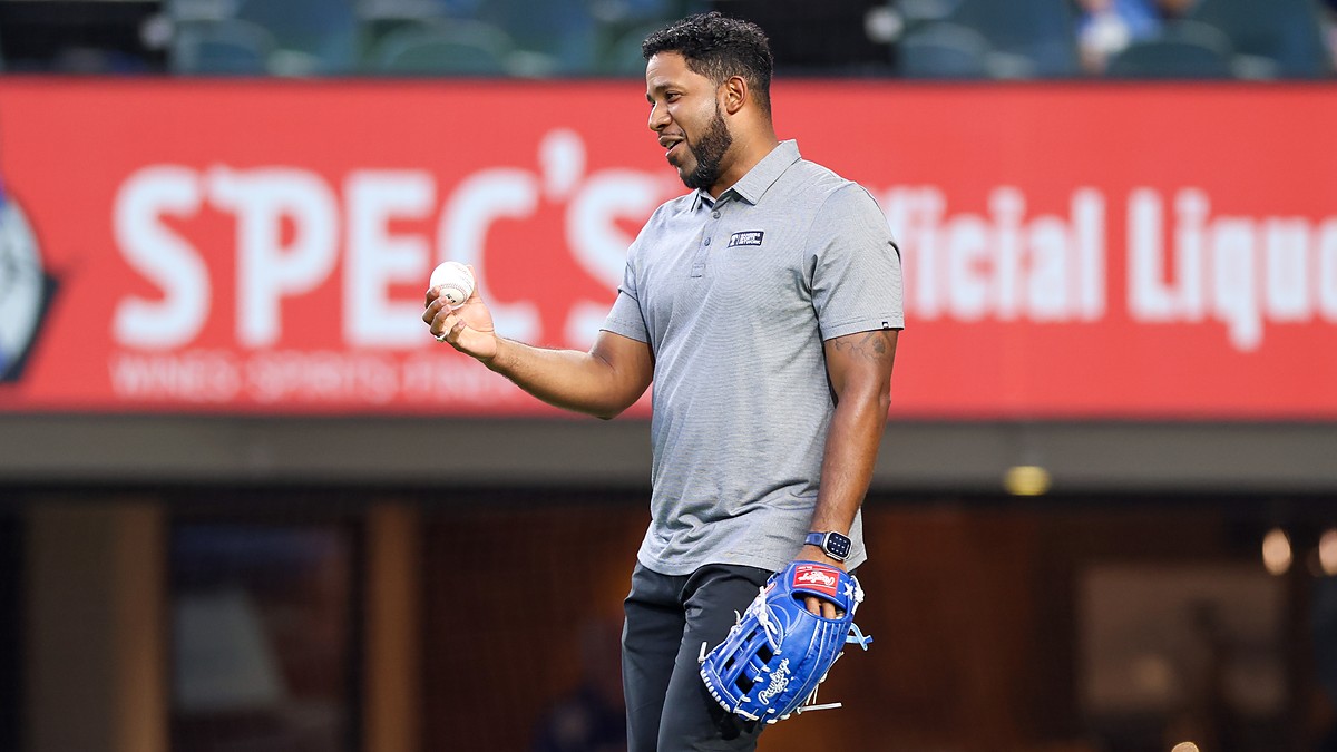 Former Texas Rangers shortstop Elvis Andrus smiles while holding a baseball and wearing a blue glove on the field.