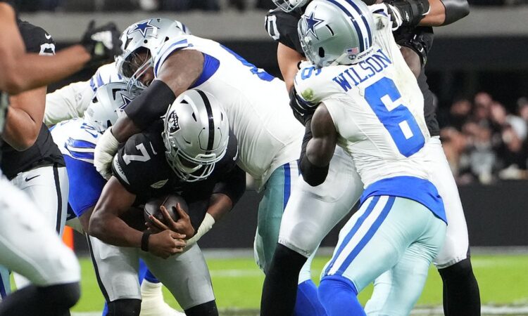 Las Vegas Raiders quarterback Geno Smith, No. 7, is wrapped up by two Dallas Cowboys defensive tackles.