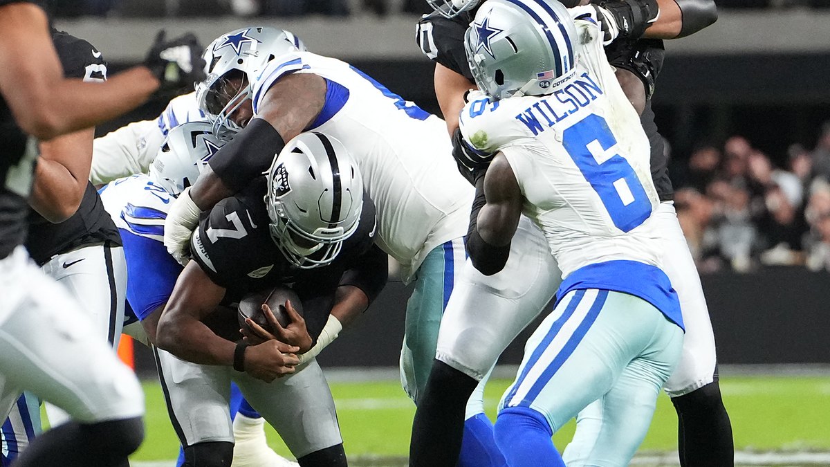 Las Vegas Raiders quarterback Geno Smith, No. 7, is wrapped up by two Dallas Cowboys defensive tackles.